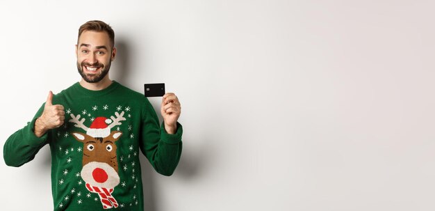 Free photo christmas holidays and shopping concept happy bearded man showing credit card and thumb up recommend