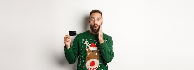 Free photo christmas holidays and shopping concept man showing credit card and looking surprised standing over