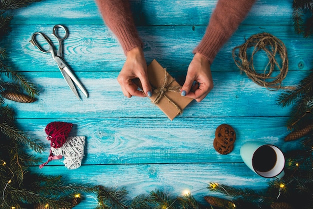 Christmas items on a blue wodden table. Woman's hands wrapping Christmas gift.