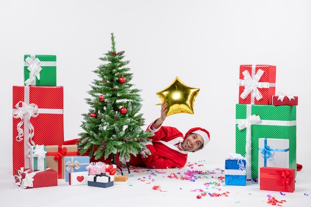 Christmas mood with santa claus lying behind christmas tree near gifts in different colors on white background