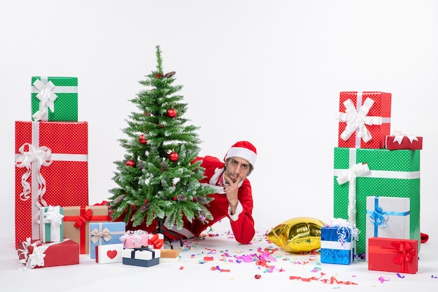 Christmas mood with young santa claus hiding behind christmas tree near gifts in different colors on white background image