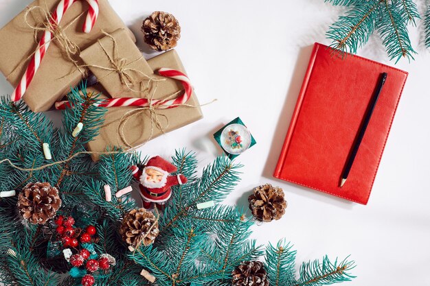 Christmas or New Year background: fur-tree, branches, gifts, decoration, red notebook with pen on a white background