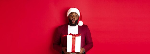 Christmas new year and shopping concept surprised african american man in santa hat saying wow holdi