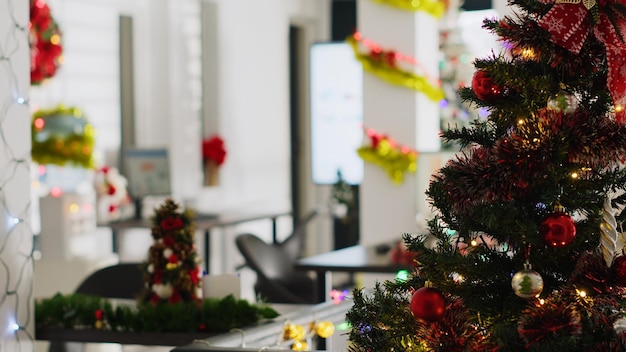 Free Photo christmas pine tree adorn with garlands and baubles in empty office. business revenue forecasts on computer screens in xmas adorn workplace with no workers during winter holiday season