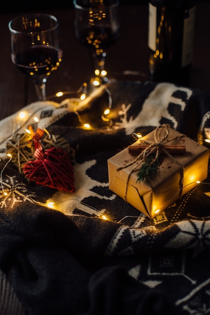 Christmas present with knitted sweater, Christmas lights and two glasses of wine.