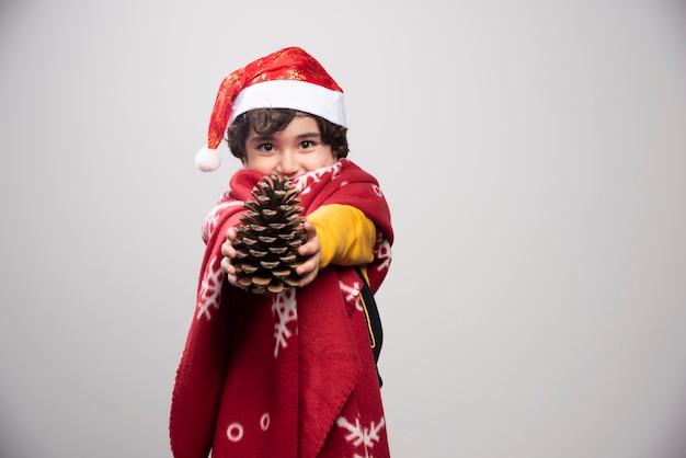 Free photo christmas time with kid disguised in red santa claus uniform offering pinecone