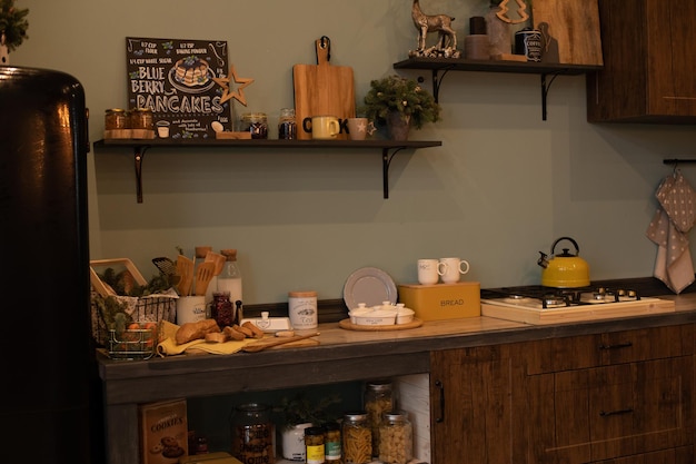 Christmas wreath and fir tree branches in vases and cups all around the modern kitchen. Modern kitchen with black fridge decorated for Christmas and New Year.