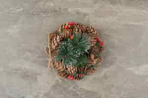 Free photo christmas wreath with red beads and cones on marble.