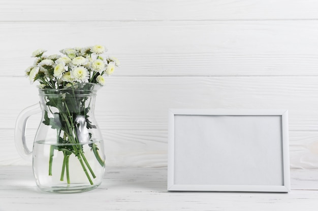 Free photo chrysanthemum flower in the glass jug against blank frame on wooden backdrop