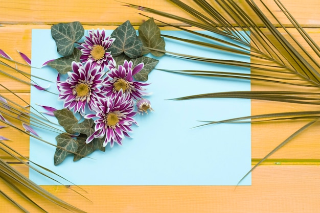 Free Photo chrysanthemum flower with ivy and palm leaves on blank paper over the wooden background