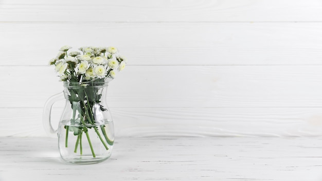 Free Photo chrysanthemum flowers inside the glass jug against white wooden background