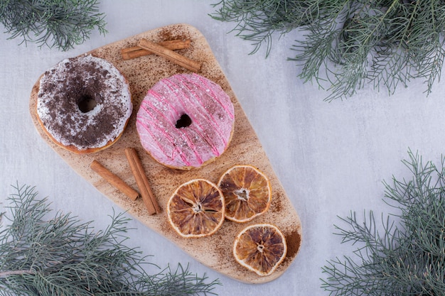 Cinnamon sticks, donuts and dried orange slices on a board on white background.