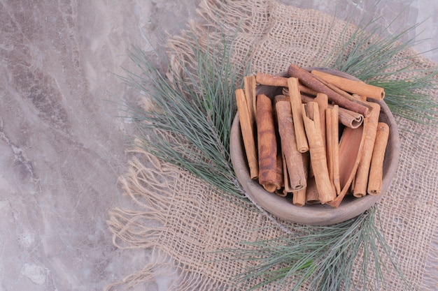 Free Photo cinnamon sticks in a wooden cup with oak tree branch around