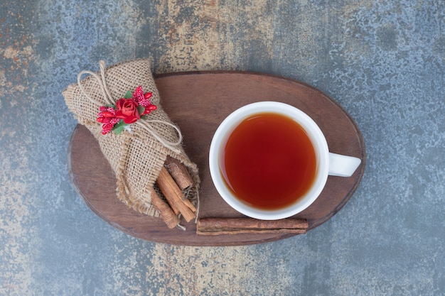 Free photo cinnamons in burlap and cup of tea on wooden plate. high quality photo