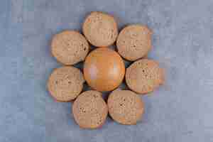 Free photo circle of brown bread slices around a single bun on marble background. high quality photo