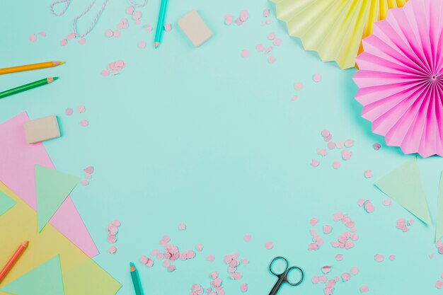 Circular paper fan with confetti and colored pencils on teal background