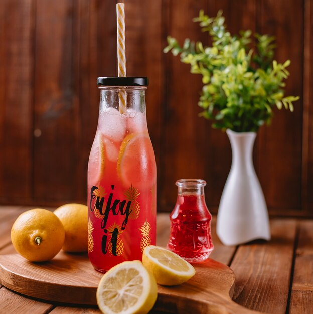 Citrus cocktail with lemon slices and red syrup in bottle with straw pipe