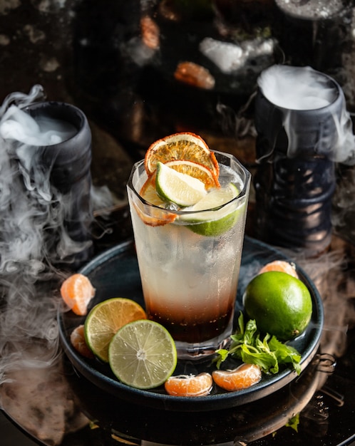 Citrus cocktail with orange and lime slices around smoked glasses