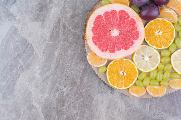 Citrus fruits, plums and grapes on wood piece. 