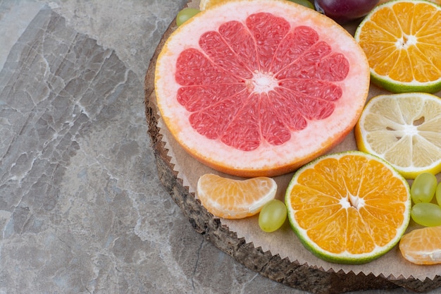 Citrus fruits slices and grapes on wood piece. 