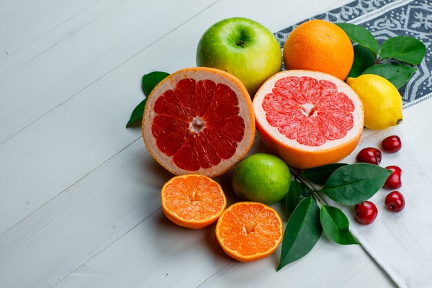 Citrus fruits with apple, cherries, leaves high angle view on wooden and tea towel table