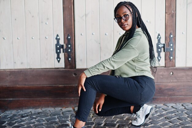 City portrait of positive young dark skinned female wearing green hoody and eyeglasses