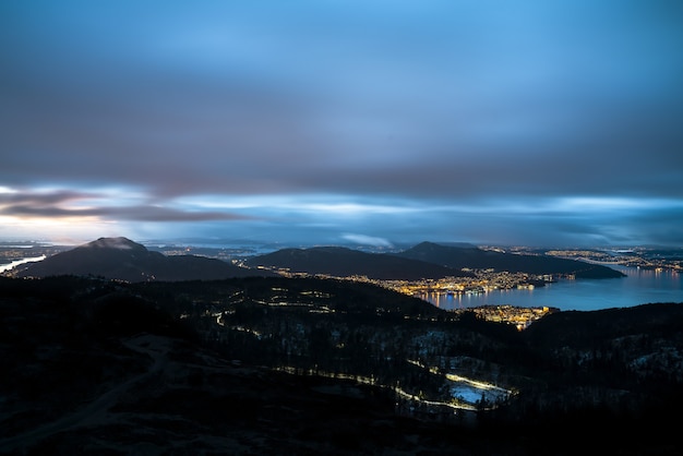 Free Photo city surrounded by mountains and a sea covered in lights under a cloudy sky in the evening