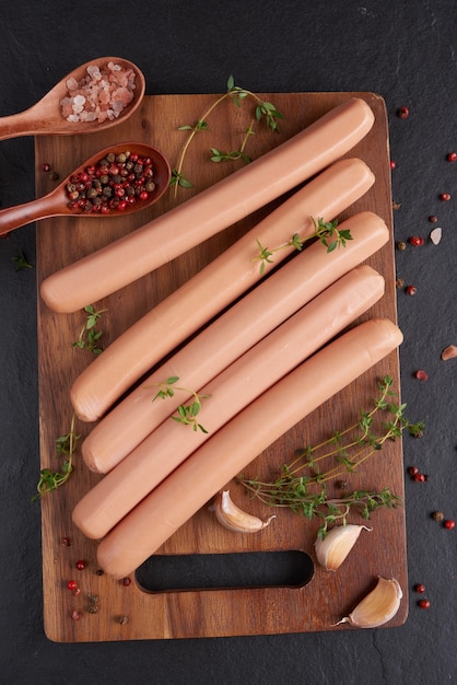 Classic boiled meat pork sausages on chopping board with pepper and basil, parsley, thyme and cherry tomatoes.