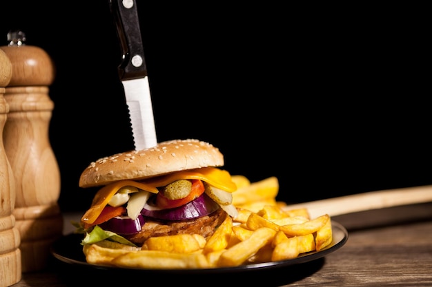 Free photo classic home made cheesburgers on black plate and background next to fries. fast food. unhealthy snack