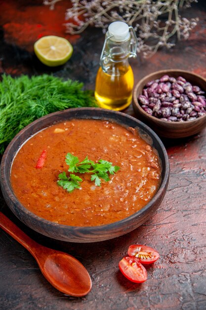 Classic tomato soup in a brown bowl beans and spoon oil bottle on mixed color table