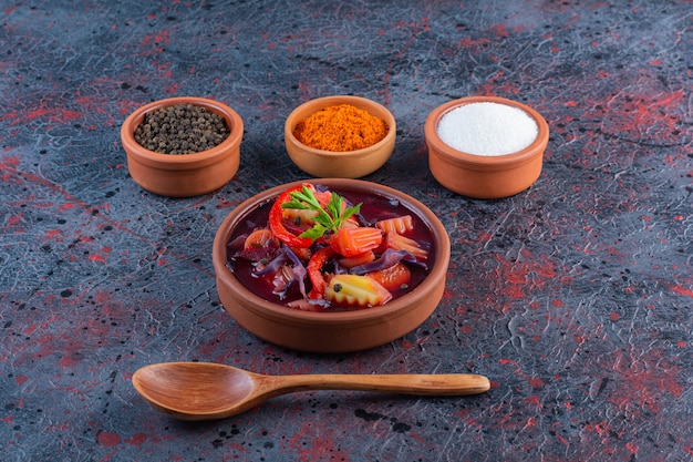 Free photo clay bowl of fresh vegetable soup with condiments on marble surface