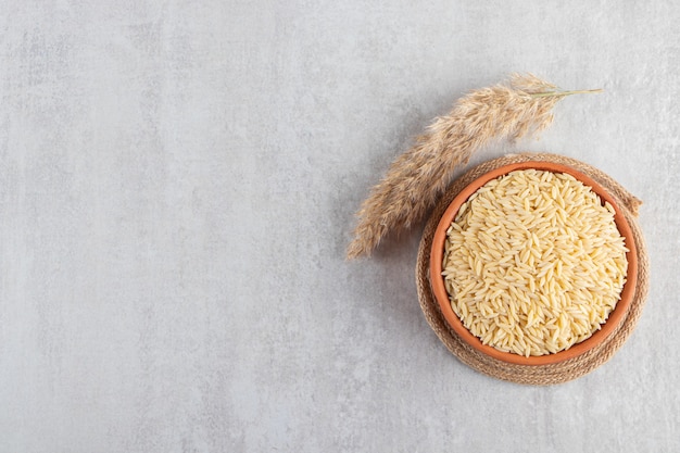 Clay bowl full of raw rice placed on stone background. 