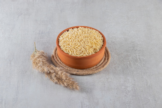 Clay bowl full of raw rice placed on stone background. 