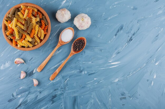 A clay bowl of multi colored raw spiral pasta with garlic and spices.