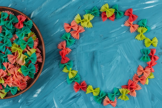 Free Photo clay plate of colorful raw farfalle pasta on blue background. 