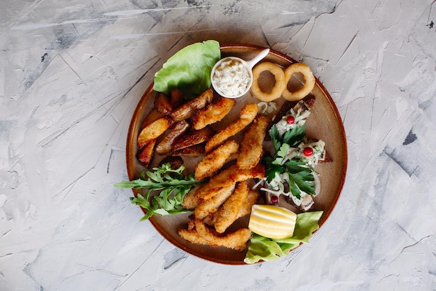 Clay plate full of appetizers including goldy chicken nuggets with chrispy crust delicious canapes with herring and cherry tomatoes served with garlic sauce decorated with salad leaves and cheese