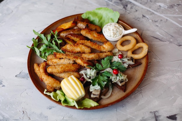 Clay plate full of appetizers including goldy chicken nuggets with chrispy crust delicious canapes with herring and cherry tomatoes served with garlic sauce decorated with salad leaves and cheese