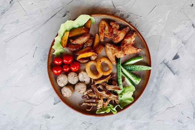 Clay plate full of appetizers including goldy chicken nuggets with chrispy crust delicious canapes with herring and cherry tomatoes served with garlic sauce decorated with salad leaves and cheese