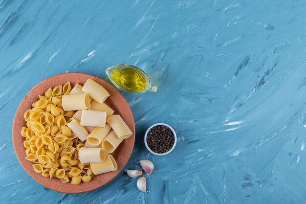 A clay plate of uncooked pasta with oil and fresh red tomatoes on a blue background . 