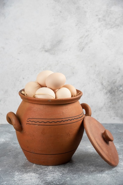 Clay pot full of raw chicken eggs on marble.