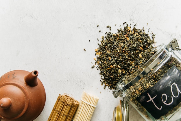 Free Photo clay teapot; rolled up placemat with spilled dried herbal tea spilled from glass jar