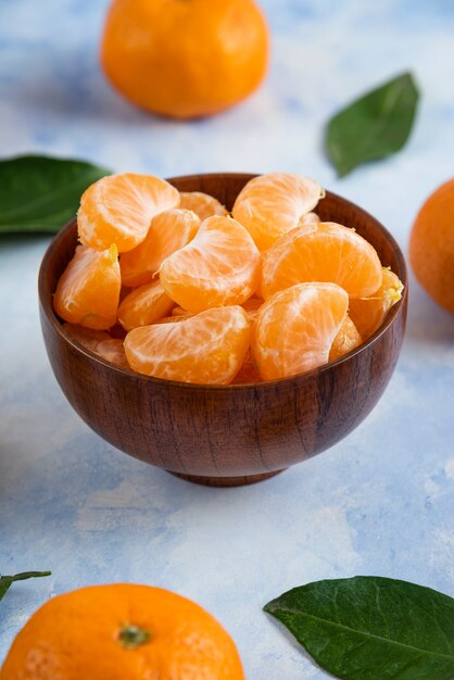 Clementine Mandarin slices in wooden bowl on blue surface