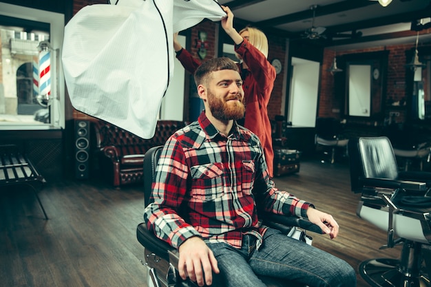 Free Photo client during beard shaving in barbershop. female barber at salon. gender equality. woman in the male profession.