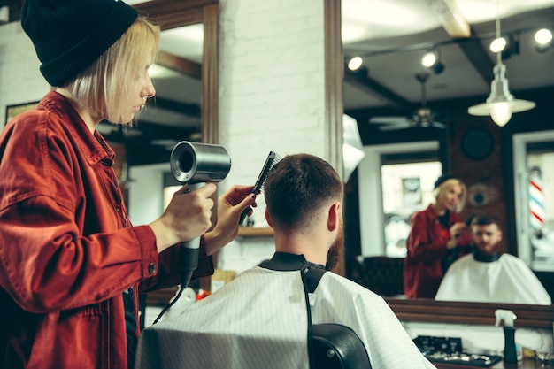 Client during beard shaving in barbershop. Female barber at salon. Gender equality. Woman in the male profession.