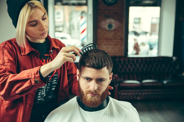 Client during beard shaving in barbershop. Female barber at salon. Gender equality. Woman in the male profession.