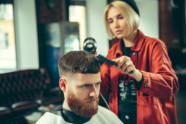 Client during beard shaving in barbershop. Female barber at salon. Gender equality. Woman in the male profession.