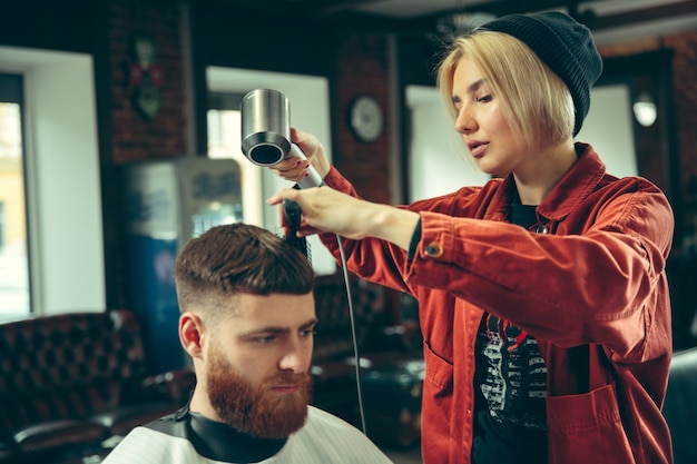 Client during beard shaving in barbershop. Female barber at salon. Gender equality. Woman in the male profession.