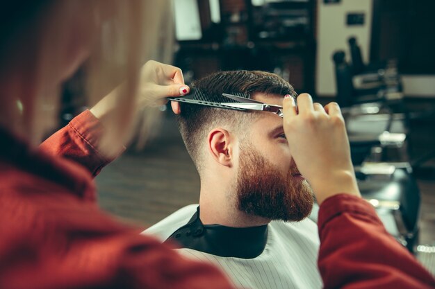 Client during beard shaving in barbershop. Female barber at salon. Gender equality. Woman in the male profession.