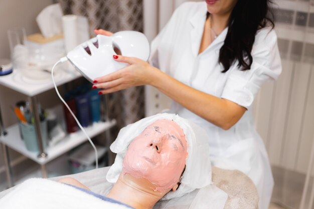 The client lies in the salon on the cosmetology table with a white mask on her face