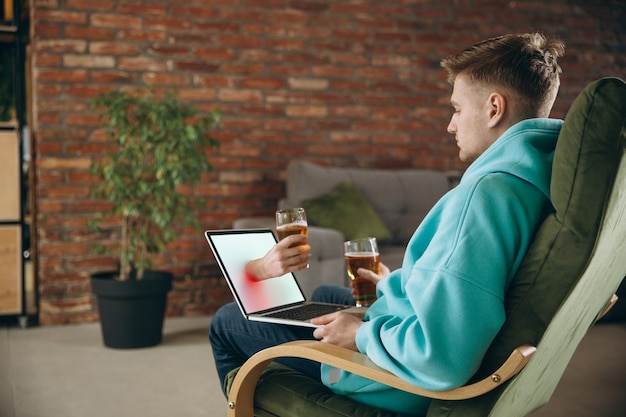 Free Photo clinking. young man drinking beer during meeting friends on virtual video call. distance online meeting, chat together on laptop at home. concept of remote safe meetings and entertainment.